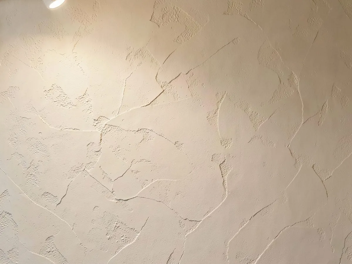 Off-white textured decorative plaster wall with trowelled surface relief under side lighting